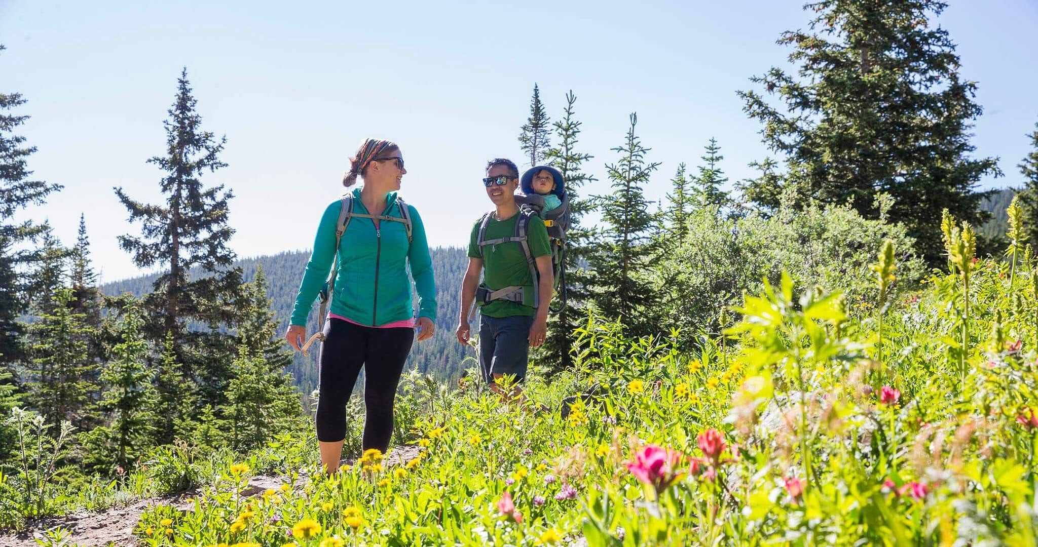 Parents hiking and carrying their child among wildflowers
